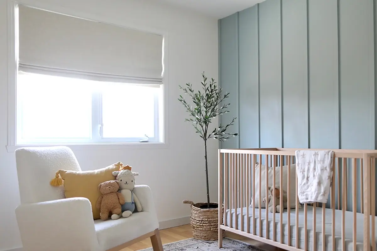 A tan-colored linen flat roman shade covers a large window in a modern nursery 