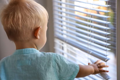 A toddler reaches for aluminum blinds