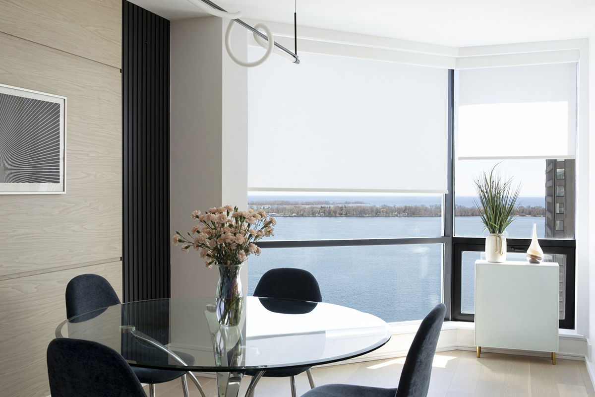 Floor-to-ceiling windows are covered with light-filtering roller shades in white in a modern apartment look out over the water