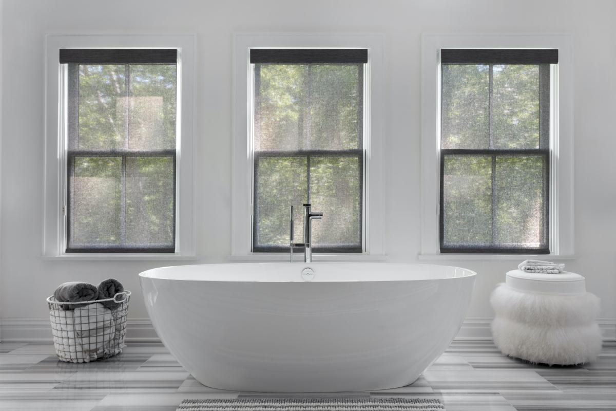 Solar shades offer partial privacy in a modern bathroom with a large freestanding tub